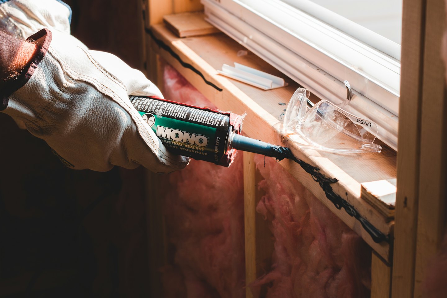 Une main gantée applique du mastic sur le nouveau cadre d'une fenêtre.