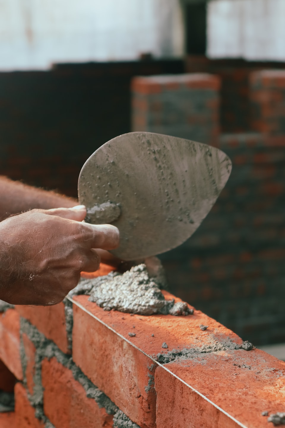 Des mains appliquent du mortier sur des briques rouges pour construire un mur.
