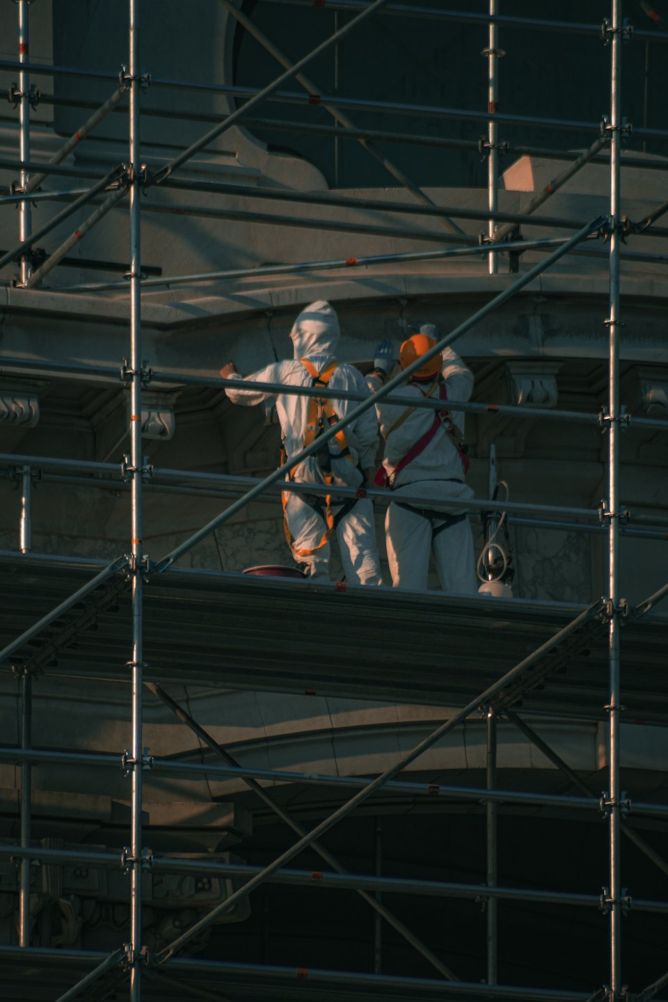 Des ouvriers en combinaison de protection sur un échafaudage réparent la façade d'un bâtiment en pierre.